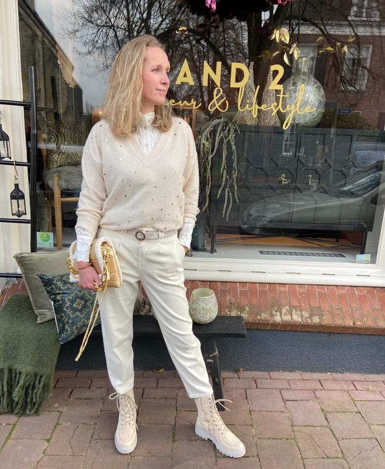 Model draagt witte outfit: witte blouse met pullover en boots.